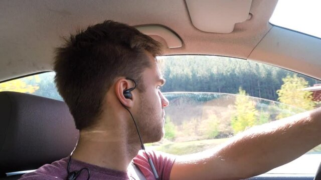 Man driving a car, handsfree headset in his ears, on the countryside of Bulgaria, on a sunny, autumn day - Handheld shot