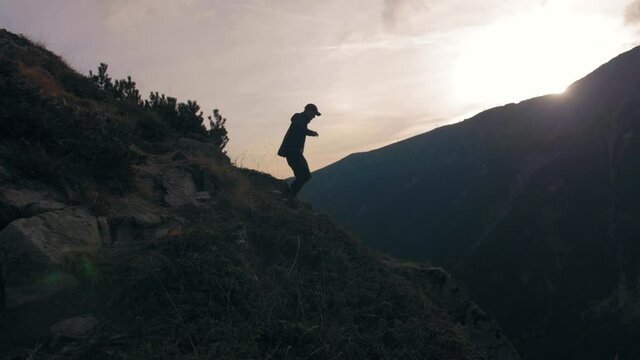 Hiker jumping down from a cliff, on a mountain trail, sunny, fall evening, in Bulgaria - Slow motion, pan view