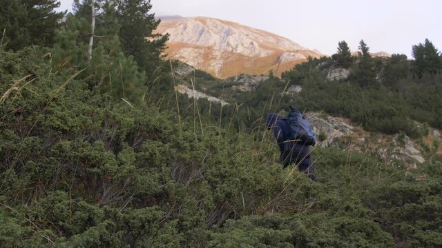 Looking up on a hiker, climbing up a mountain trail towards the summit, on a sunny, fall evening, in Bulgaria - Handheld view