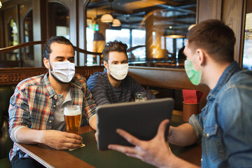 people and pandemic concept - male friends with tablet pc computer drinking beer at bar or pub