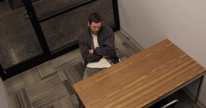 Impatient Young White Man Sitting Alone in an Interrogation Room.