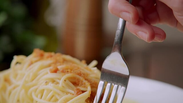 Silver fork with Caucasian finger lifts up delicious tasty traditional Italian cooked pasta dish, Spaghetti alla bottarga, delicacy of salted, aged, cured mullet fish roe, detail close up slow motion