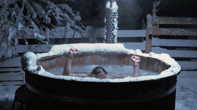 Man diving in a cold bath in a outdoor pool, full of ice. on a dark, winter evening- Still, slow motion shot