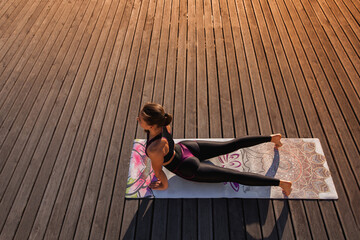 Beautiful flexible girl doing yoga at sunset near the lake on a wooden pis