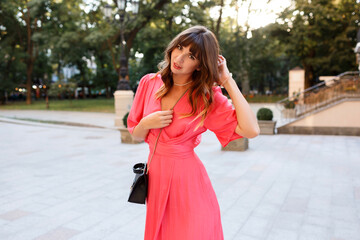 Outdoor summer portrait of elegant fashionable woman in romantic  pink dress posing in city center, Sunset colors.