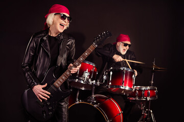 Photo of two aged pensioner lady man rock group perform concert play drum instruments solo guitar hobby bring money wear trendy rocker leather outfit bandana isolated black color background