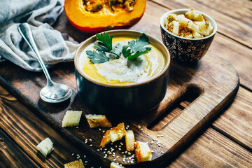 a plate of pumpkin soup on a background of pumpkin and bread crumbs on a dark wooden table