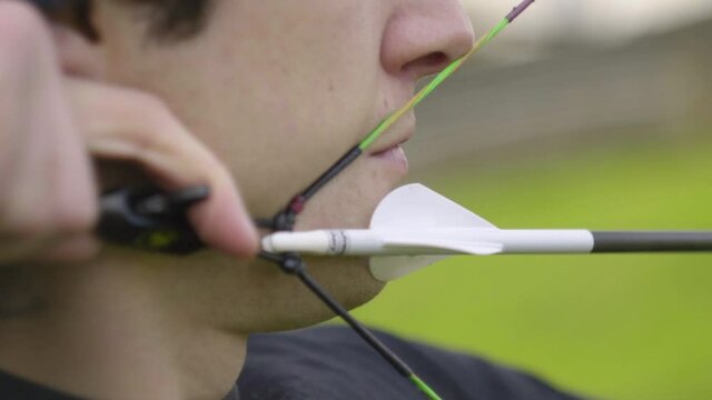 A close up shot of a nocked arrow with the compound bow at full draw. The focus is on the fletching and the string is released in slow motion.