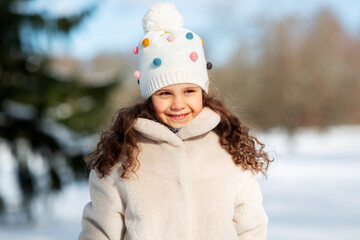 childhood, leisure and season concept - portrait of happy little girl in winter clothes outdoors at park