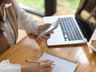 Female student searching information on mock up smartphone and write it down in notebook