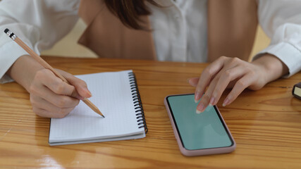 Female student looking for an idea on mock up smartphone and write it down