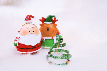 Santa Claus with christmas tree and reindeer Rudolph on snowy white background. Santa Claus in traditional red costume with reindeer Rudolph stand near handmade christmas tree. Festive decor.