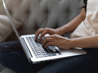 Female hands typing on laptop keyboard while relaxed sitting on sofa