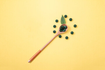 spirulina in tablets with wood spoon and jar on yellow background. Concept natural, eco, powder healthy dietary supplement