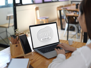 Female student doing assignment with mock up laptop in cafe