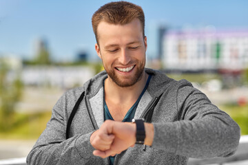 sport, technology and healthy lifestyle concept - happy smiling young man with fitness tracker in city