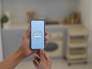 Hands holding mock up smartphone in blurred kitchen room background