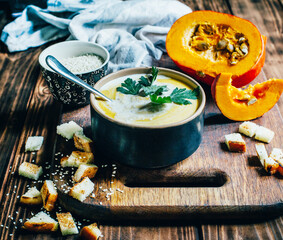 a plate of pumpkin soup on a background of pumpkin and bread crumbs on a dark wooden table