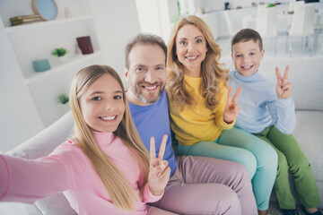 Photo of positive people family sit couch mom dad two little kids make v-sign take selfie in house indoors