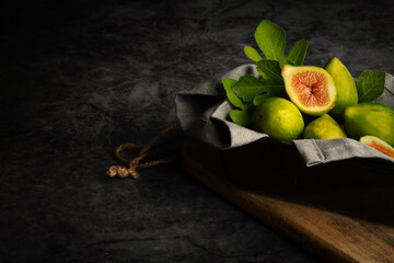 Baroque still life of basket of whole figs with one open. Decorated with napkin and leaves. Dark background