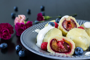 Dumplings with plums and raspberries and pink carnation flowers in the background