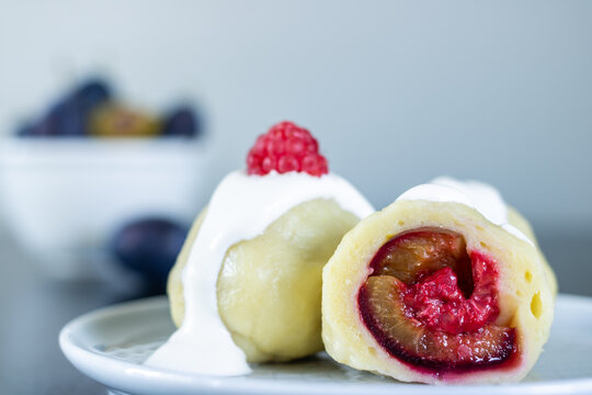 Potato dumplings stuffed with plums and raspberries, and a bowl of plums in the background