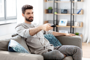 Fototapeta premium people and leisure concept - man with remote control watching tv at home