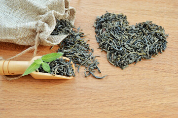 Heart made from loose leaf tea, jute bag and wooden spoon with fresh mint leaves on wooden...
