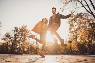 Low angle view full length photo of cheerful two young people girl guy hold hand jump in autumn...