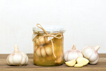 Marinated garlic in closed glass jar and fresh on wooden table Healthy fermented food Homemade pickles