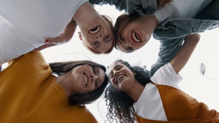 Group of women standing in a huddle and moving in a circle outdoors. Low angle view of female friends forming a huddle and smiling.
