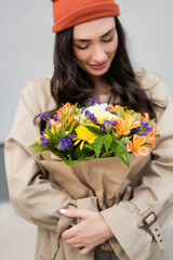 selective focus of trendy woman looking at bouquet of flowers