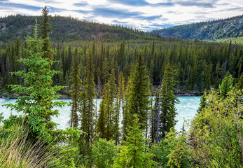 Scenic panoramic view of the Chilcotin River surrounded by pine tree forest and mountains in the background with a cloudy sky, British Columbia