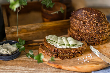 Rye whole grain bread slices with butter, fresh cucumber and salt on wooden table, country organic healthy sandwich, home kitchen, rustic style. Selective focus with copy space.
