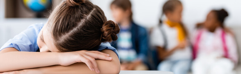 Fototapeta premium Panoramic shot of schoolgirl sleeping at desk in classroom