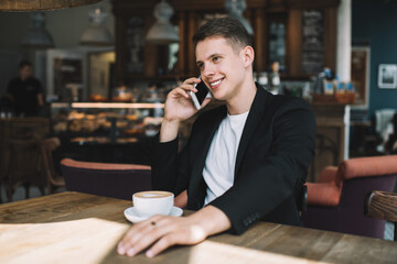 Happy young male speaking on smartphone in cafe