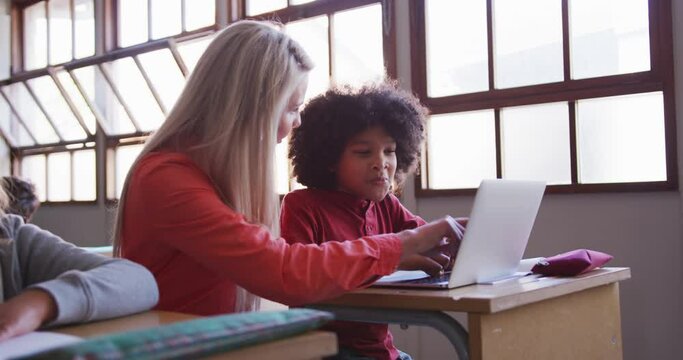 Female teacher and boy using laptop in class at school