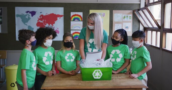 Female teacher and group of kids wearing face masks with recycle container at school - Powered by Adobe