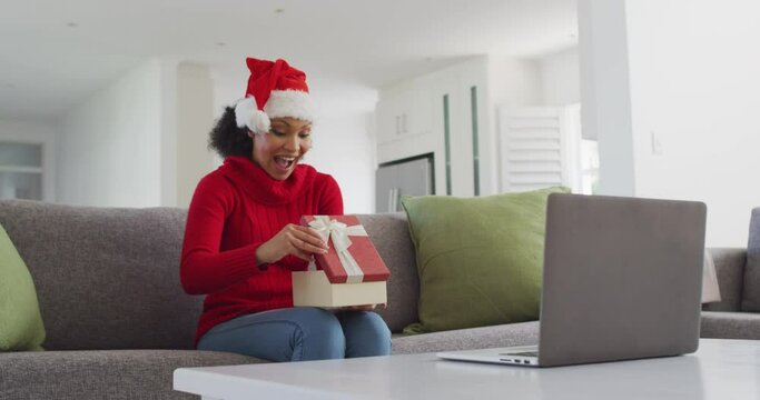 Woman Wearing Santa Hat Opening Gift Box While Having Video Chat On His Laptop