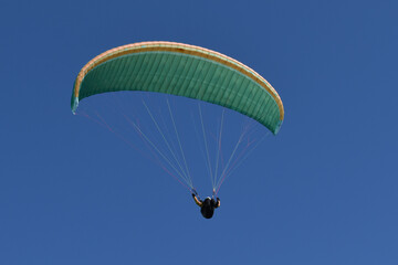 Kiteschirm in Grün und Lachsfarben vor dunkelblauem Himmel mit Kiteflieger