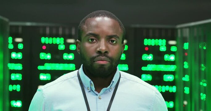 Close up of face of young African American big data office male worker looking at camera. Serious man system administrator in room with many processors. Information technology store. Portrait.