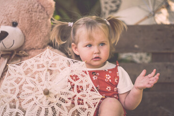 Süßes Kleinkind Mädchen mit rotem Kleid und Zöpfen großer Teddybär Sonnenschirm lächelt...