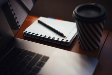 Close-up of pen and notebook on desk near laptop and coffee cup.