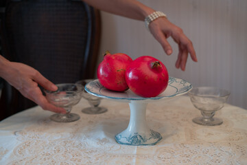 Hands setting an elegant table. Grenades and red ribbon. Traditional tablecloths and glassware for...