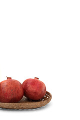two pomegranates in a wicker bowl on a white background