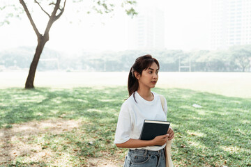 University student hold a book stand on a green field.