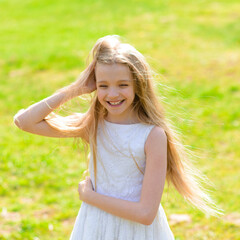 Beautiful blue-eyed girl with long blond hair in white dress walking in garden.