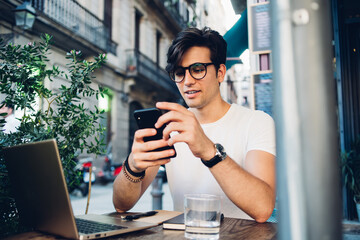 Man in glasses using smartphone at cafe