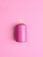 Obraz na płótnie Canvas Lit candle isolated on a pink background. Aromatic pink candle burning