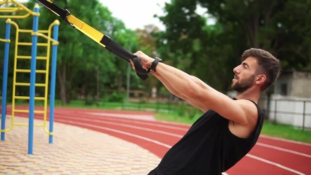 An athletic man doing push ups exercise using rubber belt to force strenth of workout on chest muscles and biceps